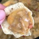 Close up of thumb holding tortilla chip scoop of best sausage dip