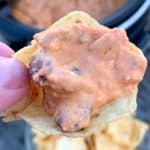 sausage and cream cheese dip on a chip held by a thumb and finger