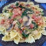 Alfredo and pesto sauce on plate of vegetable topped pasta milano