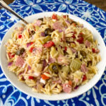 Close up bowl of easy muffuletta pasta salad in white bowl on blue and white napkin