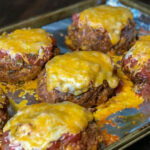 Mini taco meatloaves covered in salsa and cheese on a foil covered baking sheet