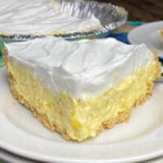 Slice of pineapple pie with a layer of Cool Whip on top on a white plate and a colorful napkin