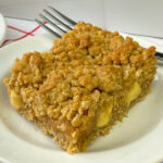 Close up caramel sauce and apple filled caramel apple bar on a white plate with the fork propped against the back of the bar