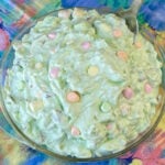 Spoon in a bowl full of green marshmallow fruit salad with colorful mini marshmallows sitting on top