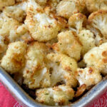 Corner of a baking sheet with parmesan coated pieces of cauliflower golden brown from roasted on a red napkin