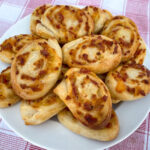 White plate of pepperoni pinwheels stacked high on a red and white napkin.