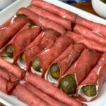 Close up of a variety of creamy dried beef and pickle roll-ups on a white plate.