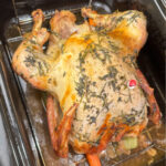 Golden brown roasted turkey breast side up covered with herbs in an electric roaster with the red thermometer popped up.