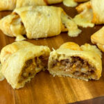 Delicious taco sticks with crescent rolls cut in half and resting on a wooden board filled with meat and cheese.