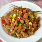 Close up meal of delicious Hawaiian spam fried rice on a white plate with a fork resting on the back.