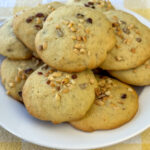Tender banana bread cookies with chopped nuts for a crunch stacked up on a white plate.