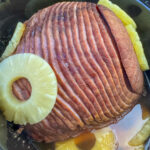 Rings of pineapple on a cooked spiral sliced ham in a large black slow cooker.
