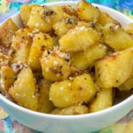 Crispy gold potatoes with honey, parmesan and garlic in a white bowl ready to serve.