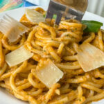 Close up fork twirling basil garlic tomato ricotta pasta around it with parmesan cheese melting on the noodles.