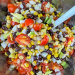 Salsa made of black beans, corn, cherry tomatoes, avocado and onions with a white handle sticking out.