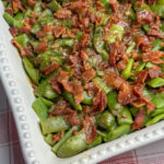 Thick green beans in a casserole dish covered with bacon and soy sauce glaze.