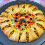 Close up of a quick taco ring meal filled with fresh chopped veggies and ready to serve on a silver baking sheet.