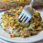 Close up of a fork in slices of zucchini and a creamy ground beef mixture with a crunchy seasoned bread stuffing casserole topping on a white plate.