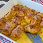 Easy apple dumplings sitting in a Mountain Dew sauce with one on a spatula ready to serve out of the white baking dish.