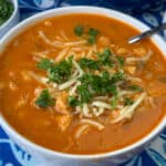 Flavorful bowl filled to the brim with crockpot white chicken chili ready to eat with cheese and parsley in the center.