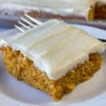 Close up of delicious carrot cake with a nice layer of frosting on a plate with a fork resting on the back of the white plate.