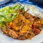 Close up plate full of a one pot rice skillet meal with plenty of savory ground beef and tomatoes garnished with lettuce and sour cream with a fork in the background.