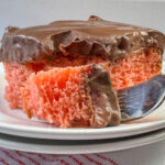 Close up of a bite of strawberry cake with a layer of fresh strawberries and chocolate on top on a stack of plates.