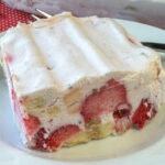 Close up piece of frozen Cool Whip and cream cheese filled with strawberries, pineapple and bananas on a white plate.