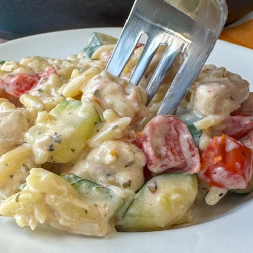 Close up of a fork scooping up a bite of creamy and delicious chicken and pasta with tomatoes and zucchini.