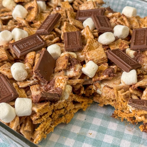 Pan full of sweet and crunchy smores cereal bars topped with chocolate and mini marshmallows in a glass dish on a teal and white napkin.