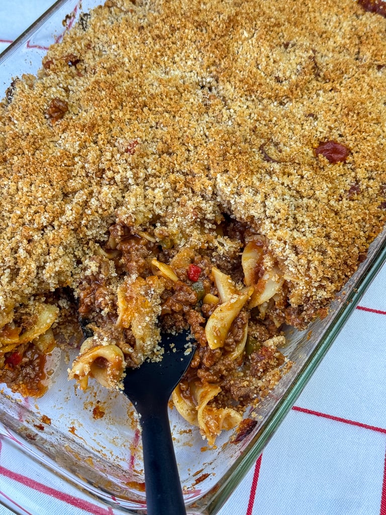 Serving spoon scooping into a flavor and easy Mexican casserole on a white napkin with red lines.