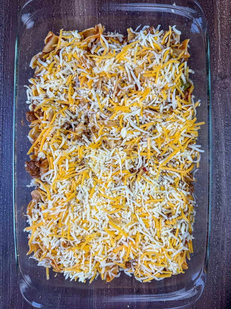 Thick layer of white and yellow Mexican cheese sprinkled over top of the meaty and saucy ground beef mixture in a 9 x 13" pan.