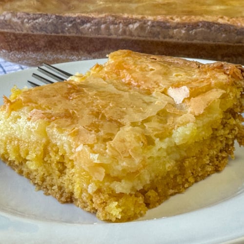 Flaky, golden brown layer of baked cream cheese and gooey butter mixture over a layer of yellow cake mix on a white plate.