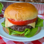 A juicy and delicious burger made on a smoker and then stacked into a cheeseburger on a premium bun on a white plate.