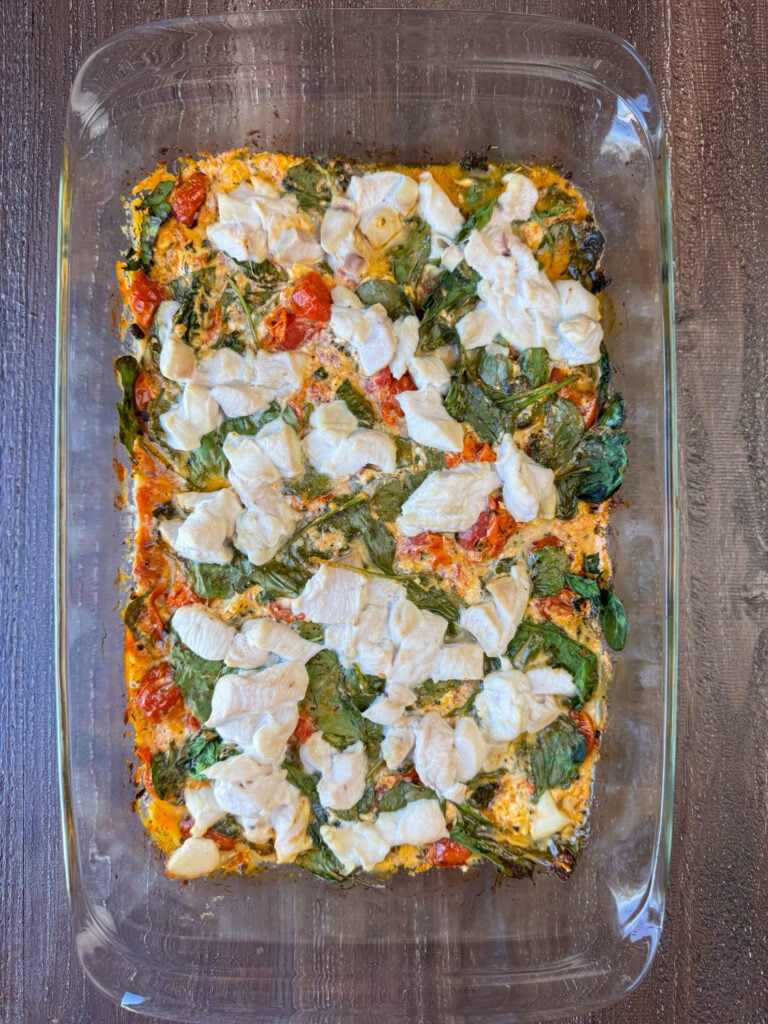Cubes of chicken baked with spinach into a feta cheese and tomato sauce in a glass baking dish.