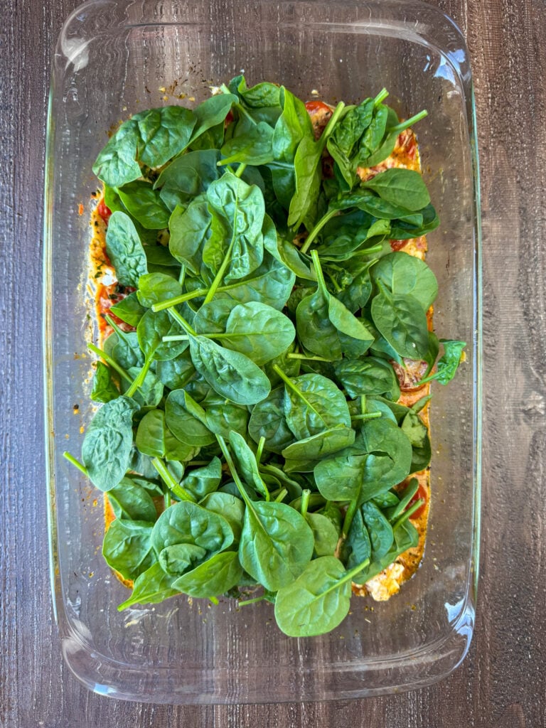 Two cups of fresh baby spinach spread over a glass 9x13 dish of baked feta pasta.