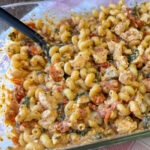 Twisted pasta coated in a distinctive deep and creamy sauce made with feta cheese and cherry tomatoes with baked chicken and spinach mixed in ready to be served with a black spoon.