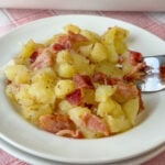Close up celery seed and bacon flavored vinegar sauce over an easy recipe for German Potato Salad with plenty of bacon on a white plate with a fork.