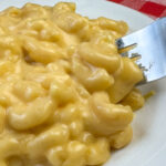 Close up fork scooping a bite of creamy no boil mac and cheese off of a white plate.