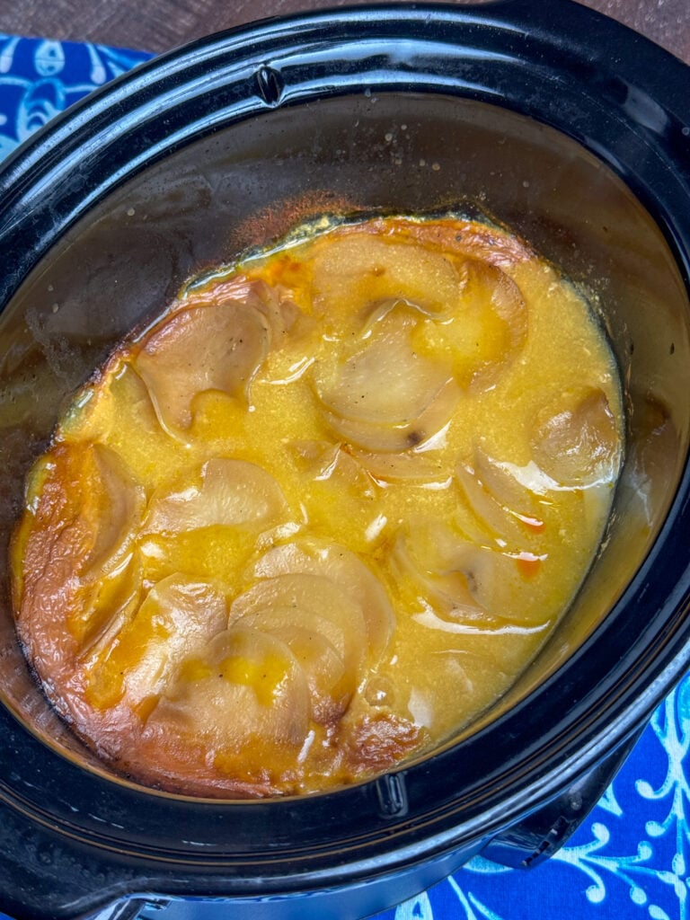 Overhead view of golden brown scalloped potatoes in a black crock on a blue and white napkin.