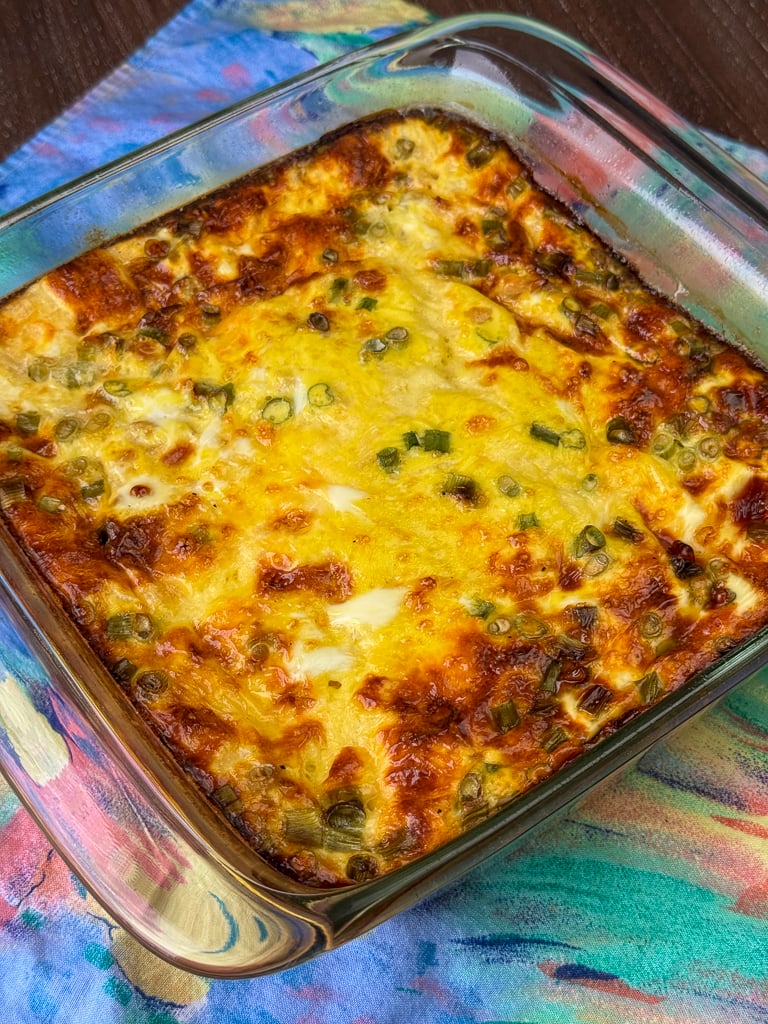 Thick, baked Farmer's Casserole in a square 8 x 8 dish with browned edges on a pastel napkin.
