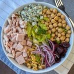 Overhead view of toppings including chopped turkey, nuts, chick peas, cranberries, and blue cheese on a lettuce salad.