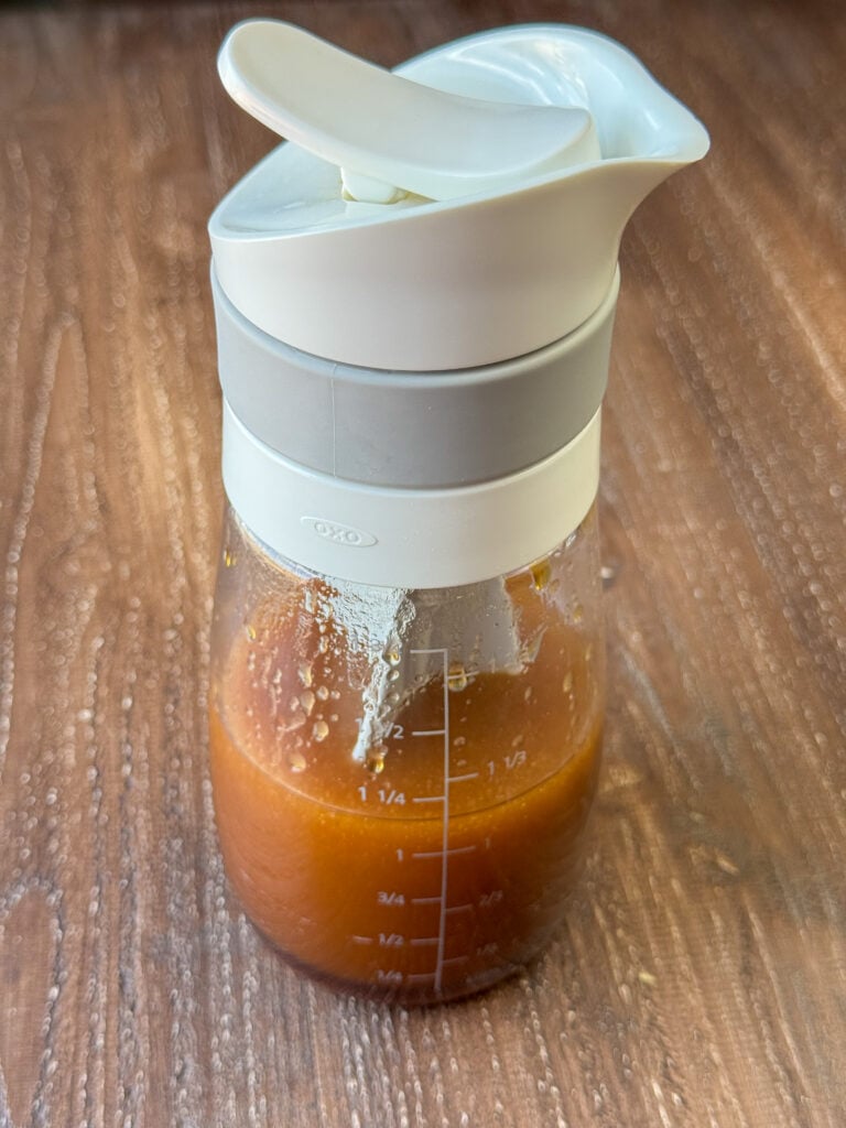 Salad dressing mixer partially full of a deep brown Asian dressing ready to pour.