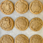Several round gingersnap cookies on a baking sheet with soft centers and a tender crumb.
