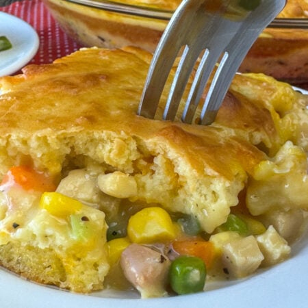 Warm and hearty serving of chicken pot pot with a thick, golden brown layer of biscuits on top of a creamy mixed vegetable and chicken layer on a white plate.