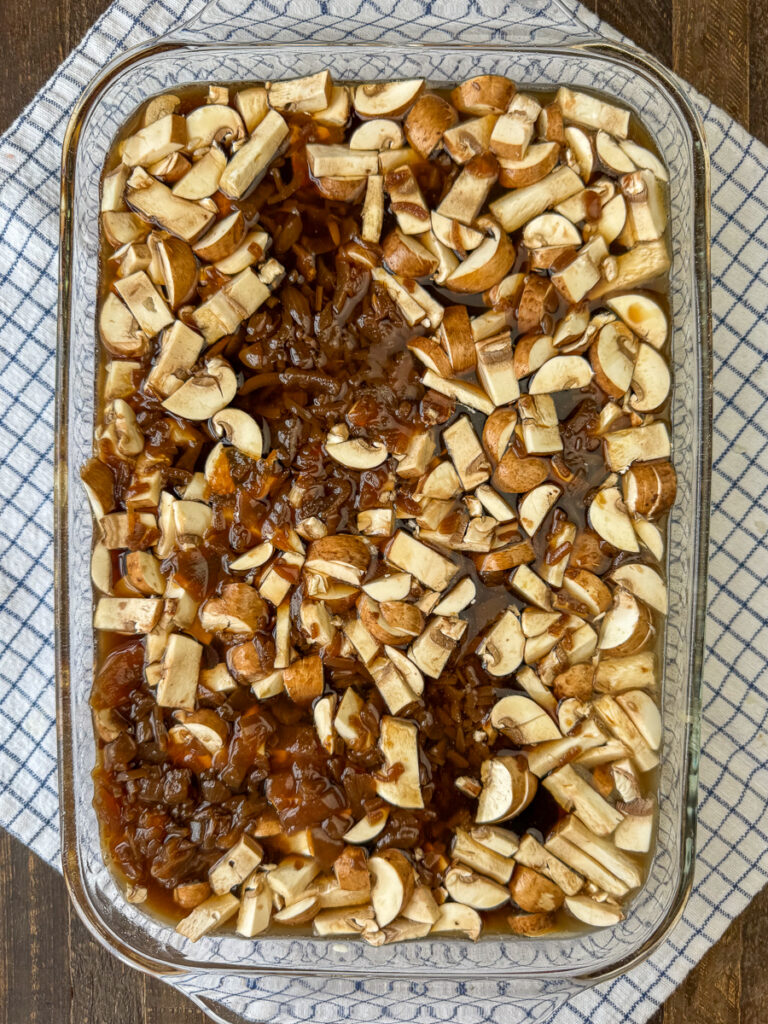 Casserole dish full of beef, rice and mushrooms with cans of French onion soup and beef Consomme poured over the top for flavor.