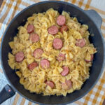 Overhead view of a skillet full of an easy kielbasa and pasta recipe with sauerkraut on a yellow and white plaid napkin.