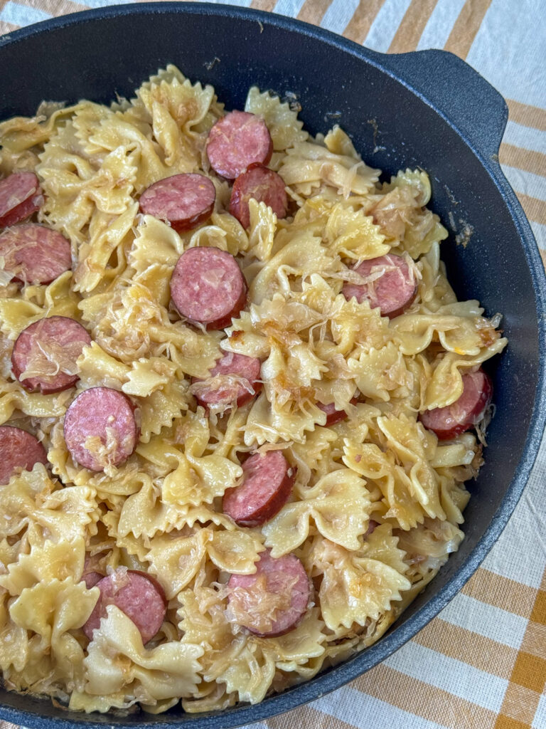 Close up non-stick skillet of noodles cooked in onions and sauerkraut with Kielbasa and Parmesan cheese added before serving.