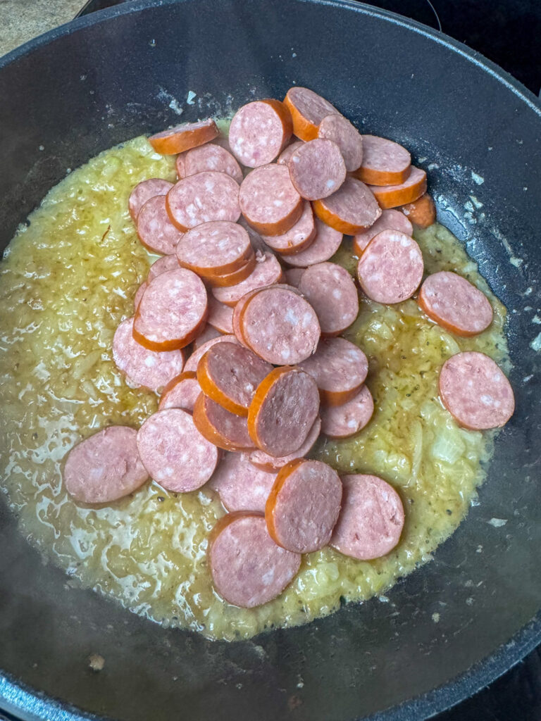 A pound of Polska Kielbasa added to a skillet with butter and onions.