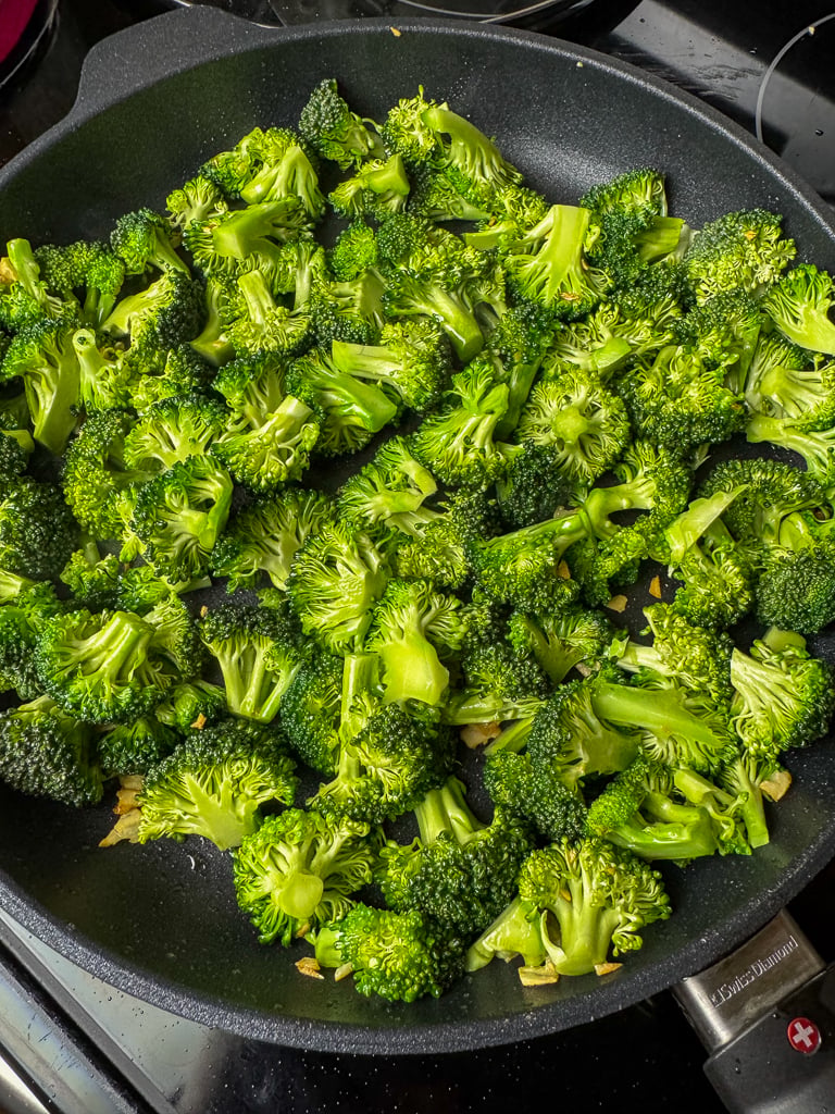Raw broccoli florets added to a hot skillet with oil.